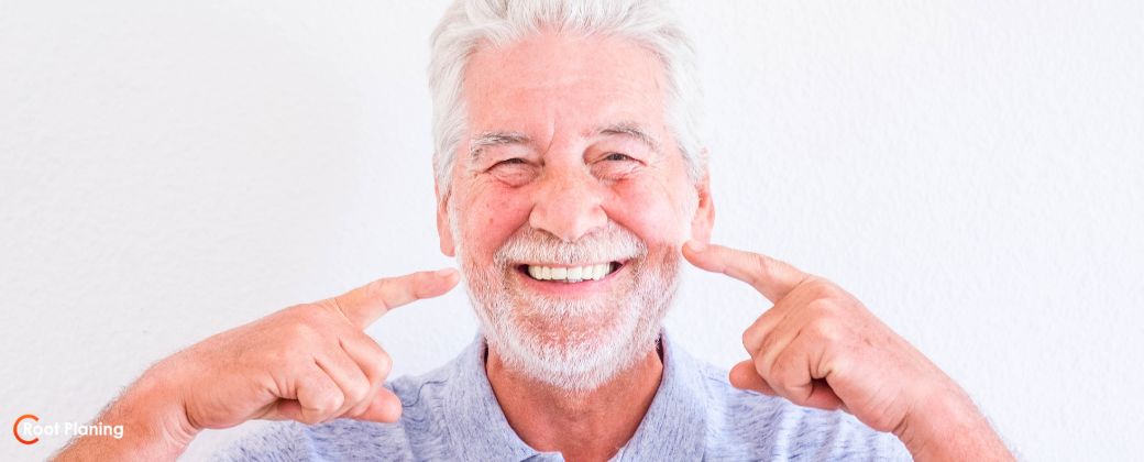גבר עם שיער לבן וזקן צרפתי מדגים האם יישור שיניים בגיל מבוגר באמת עובד. בצד שמאל למטה לוגו אתר root-planing